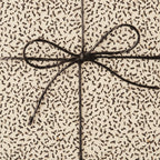 Close-up of a gift wrapped in cream paper with a brown abstract pattern, tied with a simple brown string bow.