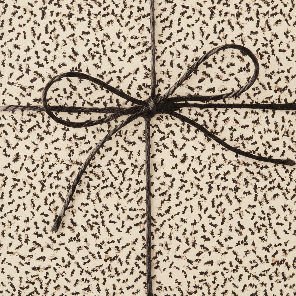 Close-up of a gift wrapped in cream paper with a brown abstract pattern, tied with a simple brown string bow.