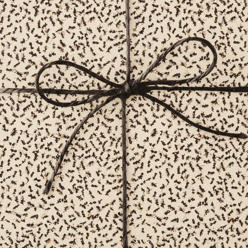 Close-up of a gift wrapped in cream paper with a brown abstract pattern, tied with a simple brown string bow.