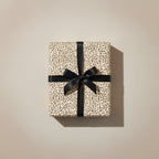 Elegant gift wrapped in minimalist cream wrapping paper with tiny dark accents, tied with a black satin ribbon.