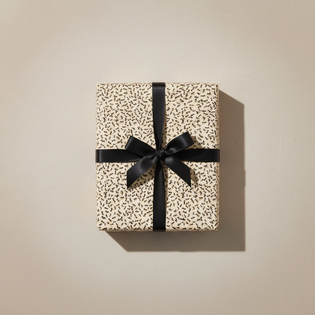 Elegant gift wrapped in minimalist cream wrapping paper with tiny dark accents, tied with a black satin ribbon.