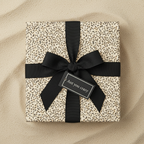 Modern gift box with black ribbon, and ant print wrapping paper on sand background.