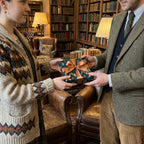 Elegant gift exchange featuring botanical print wrapping paper with a bronze ribbon in a home library setting.