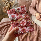 Hand holding luxury pink rose floral wrapping paper tied with gold string. Ideal for Valentine's Day or Mother's Day gifts.