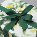 Gift box wrapped in lemon print wrapping paper with a dark green ribbon bow.