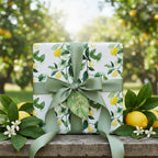 Square gift wrapped in lemon print paper with olive ribbon, set amongst an orchard backdrop.