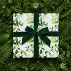 Elegant gift wrapped in white lemon floral wrapping paper with green velvet ribbon on a botanical background.