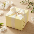 Pale yellow wrapping paper on a square gift box tied with a cream-colored ribbon and bow.