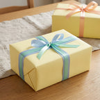 Solid yellow gift box with blue ribbon, wrapped in pastel wrapping paper, perfect for birthday or baby shower.