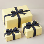 Three pastel yellow gift boxes wrapped with elegant navy blue linen ribbon bows.