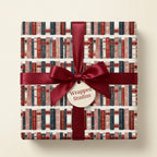 Vintage bookshelf wrapping paper on a gift box with a burgundy satin bow by Wrapped Studios.