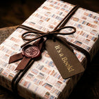 Vintage bookshelf wrapping paper on a gift with leather cord and 'It's a Book!' tag, by Wrapped Studios.