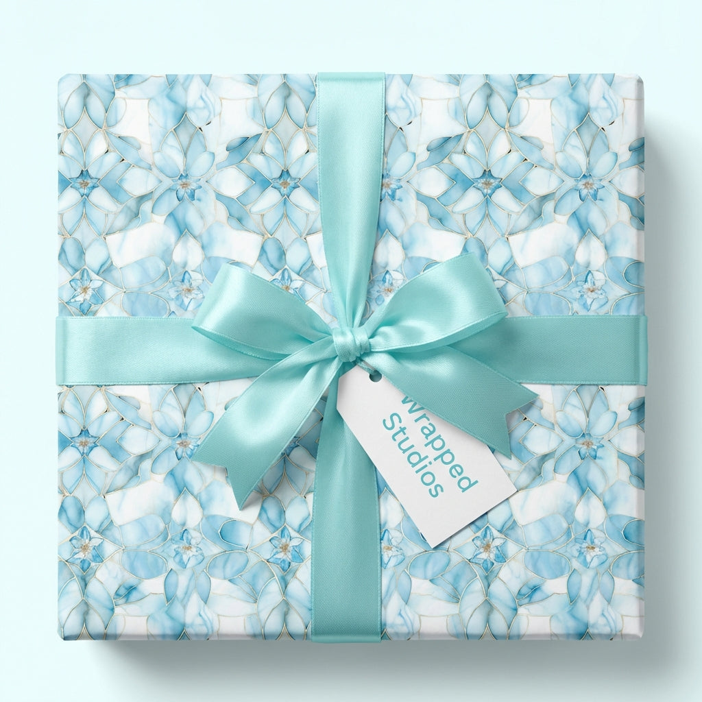Light blue floral mosaic wrapping paper on gift box with blue floral pattern and a turquoise ribbon, featuring 'Wrapped Studios' tag.