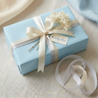 Light blue wrapping paper on a rectangular gift box with cream and silver ribbon, baby blue tag and white flowers.