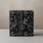 Elegant gift box wrapped in luxury black floral wrapping paper with silver ribbon and tag.
