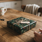 Square gift wrapped in dark green floral Christmas wrapping paper with twine and a "For You" tag.