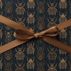 Elegant gift wrap featuring a gold beetle pattern on a dark blue background, tied with a brown satin ribbon.