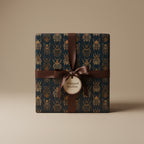 Elegant gift box wrapped in dark teal wrapping paper with gold beetle pattern and brown satin ribbon.