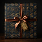 Elegant gift wrapped in dark wrapping paper with a gold beetle pattern and satin bronze ribbon.