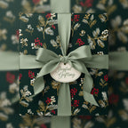 Dark green Christmas wrapping paper with red berry and gold foliage pattern, tied with sage green ribbon.