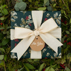 Elegant Christmas gift wrapped in dark green floral wrapping paper with a cream ribbon and "For You" tag.