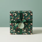 Elegant Christmas gift wrapped in floral holly berry paper, tied with a green satin ribbon and a "Joy" tag.