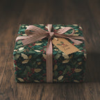 Square gift wrapped in green holly berry Christmas gift wrap with a striped ribbon and "With Love" tag.