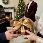 Burgundy Christmas gift wrap with gold ornaments and satin bow being exchanged.