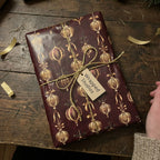 Burgundy Christmas gift wrap from Wrapped Studios with a gold ornament pattern and twine bow.