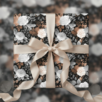 Elegant floral wrapping paper with white and bronze roses on a black background, finished with a satin ribbon.