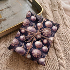 Elegant Christmas gift wrap with a vintage ornament pattern and copper twine on a cozy knit blanket.