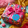 Colorful macaron print wrapping paper on a gift box with a pink satin ribbon and "Sweet Treats!" tag.