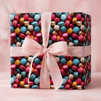 Square gift box with colorful macarons wrapping paper and a light pink satin ribbon and bow.