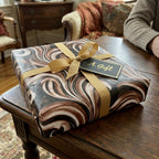 Brown marble luxury gift wrap with a gold ribbon and gift tag on a box by Wrapped Studios.