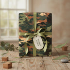 Rectangular gift wrapped in camouflage paper with a sage green ribbon on a wooden table.