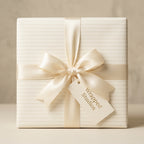 Elegant cream pinstripe wrapping paper by Wrapped Studios, featuring an ivory satin bow for luxury wedding gifts.