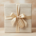 Elegant cream wrapping paper with subtle wave pattern, tied with a luxurious gold satin ribbon and bow.