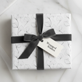 Elegant white wrapping paper with a minimalist black leaf pattern and a charcoal grey velvet ribbon, perfect for luxury gifts.