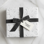 Elegant white wrapping paper with a minimalist black leaf pattern and a charcoal grey velvet ribbon, perfect for luxury gifts.
