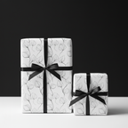 Elegant white floral wrapping paper with delicate black leaf illustrations and a black ribbon, perfect for luxury gifts.
