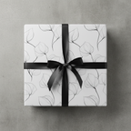 Elegant minimalist floral wrapping paper with delicate black leaf outlines and a sleek black satin ribbon bow on a gray background.