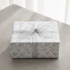 Elegant minimalist gift wrap with a delicate black botanical leaf pattern on white paper, tied with a sheer silver ribbon.