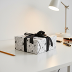 Elegant floral wrapping paper with black ribbon, perfect for luxury gifts or birthday presents on a minimalist desk.