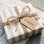 Neutral striped wrapping paper by Wrapped Studios on a rustic gift box with a twine bow and Cheers tag.