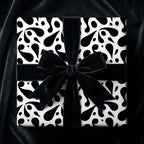 Luxury black and white gift wrap with an abstract paisley drop pattern and a large black velvet bow on a square box.