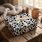 Black and white paisley wrapping paper on a gift box with a beige ribbon, set on a cozy rustic wooden table.