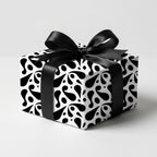 Elegant black and white abstract patterned wrapping paper on a square gift box, tied with a black satin ribbon bow for a modern look.
