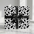Luxury black and white abstract paisley patterned wrapping paper with a black satin bow, tied on a square gift box.