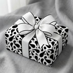 Modern black and white abstract paisley wrapping paper on a luxury gift box tied with a white ribbon bow with black trim.
