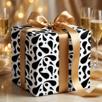 Modern black and white abstract pattern wrapping paper tied with a luxurious gold satin ribbon for a sophisticated celebration.